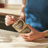 Together Health Mushroom 5; sinisessä paidassa oleva henkilö avaa mattapintaisen ruskean taipuisan pussin tekstillä ”Together Health Organic Mushroom 15” lihavoidulla valkoisella ja vihreällä groteskitekstillä, vaalealla keittiön työtasolla; pakkaus suorakaiteen muotoinen uudelleensuljettavalla reunalla, ei näkyvää ikkunaa tai grafiikkaa; henkilö avaa ruskean pussin korostaen luonnonmukaisia ainesosia vaalealla työtasolla.