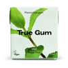 True Gum -pakkaus, merkintä muoviton ja vegaaninen, minttumaku, sokeriton, paino 21 g; suorakaiteen muotoinen pakkaus mattavalkoisella pinnalla ja vihreillä minttulehtikuvituksilla etusivulla; päätekstissä lihavoitu musta groteskikirjasin, lisämerkinnät kevyemmällä fontilla; ei ihmisiä tai käsiä näkyvissä; tausta valkoinen, kuvattu suoraan edestä silmän tasolta.