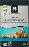Rectangular box labeled “Urtekram Organic Golden Cane Sugar” in white serif and sans-serif fonts, with legible weight “500 g.” Matte finish. Photo of stacked brown sugar cubes on the front. Certification logos for organic, KRAV, and Fairtrade are displayed. Neutral background; product is photographed front-facing; no people or hands present.
