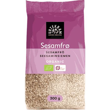 A 300g bag of Urtekram organic sesame seeds comes in purple and beige matte-finish plastic packaging. The pouch is rectangular with a flat bottom. Labels display various languages, organic certification symbols, and the bold “Urtekram” brand logo. Sans-serif fonts are used. Only product name and details are readable. Photographed against a plain white background with no people or objects present.