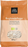 A 500g bag of Urtekram organic buckwheat flakes with a transparent window displaying the nutritious flakes inside. Rectangular, upright pouch format; packaging is matte orange with a clear section on the front. Sans-serif text in white and dark colors shows product name and multiple languages. No people, plain background, studio product shot.