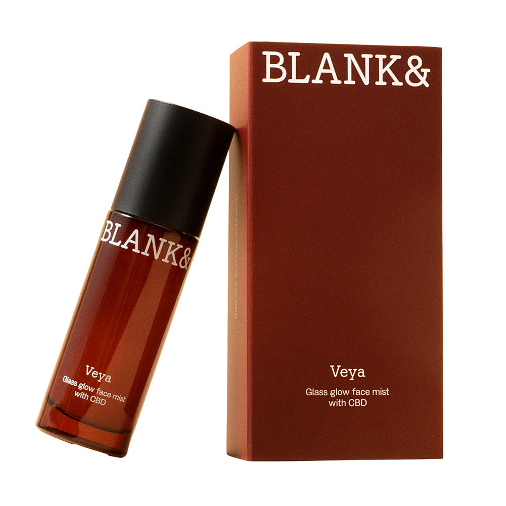 Blank& Veya Kasvosuihke; ruskea sylinterin muotoinen pullo valkoisella etiketillä tekstillä ”BLANK& Veya Glass Glow Face Mist with CBD” asetettuna vinoon, nojaten suorakulmaista rasiaa vasten; rasia samaa väripalettia ja yhtä pelkistettyä groteskikirjasinta kuin pullo; molemmat pakkaukset mattapintaisia; tausta valkoinen, ei ihmisiä tai rekvisiittaa.