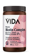 Vida Beauty Biotin Complex; ruskea muovipullo tekstillä "VIDA Beauty Biotin Complex", 5000 µg biotiinia, kalsiumia, sinkkiä ja C-vitamiinia; ravintolisä tukee paksua tukkaa ja vahvoja kynsiä; pullo sisältää 100 kapselia, etiketti pääosin valkoinen ja vaaleanpunainen; pullon pinta mattainen, lieriön muotoinen kierrekorkillinen; sans-serif-fontti hallitsee etikettiä; kuva näyttää vain tuotteen valkoista taustaa vasten, ei ihmisiä tai muita esineitä.