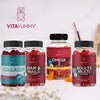 VitaYummy Collagen, maku Cherry; neljä VitaYummy-purutablettipulloa esillä valkoisella alustalla; jokainen pullo lieriömäinen, kirkasta muovia värikkäin kansin; etiketeissä tuotenimet Collagen, Hair & Nails, Omega 3 ja Adults Multi lihavoidulla groteskifontilla; hedelmänmuotoisia eriväreisiä purutabletteja hajautettuna pullojen ympärille; ei ihmisiä tai käsiä.
