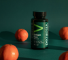 Vitalized Collagen Caps; lieriömäinen muovipullo tekstillä Vitalized Collagen Caps seisoo pystyssä sileällä, yhtenäisellä vihreällä pinnalla; neljä kuorimatonta mandariinia aseteltuna pullon ympärille; pullo mattavalkoinen tummalla kannella; etiketissä groteskitekstiä, joka kertoo hyödyistä iholle, hiuksille, kynsille ja nivelille; ei ihmisiä tai käsiä; tuotekuva kaikkien esineiden näkyessä yksinkertaista taustaa vasten.
