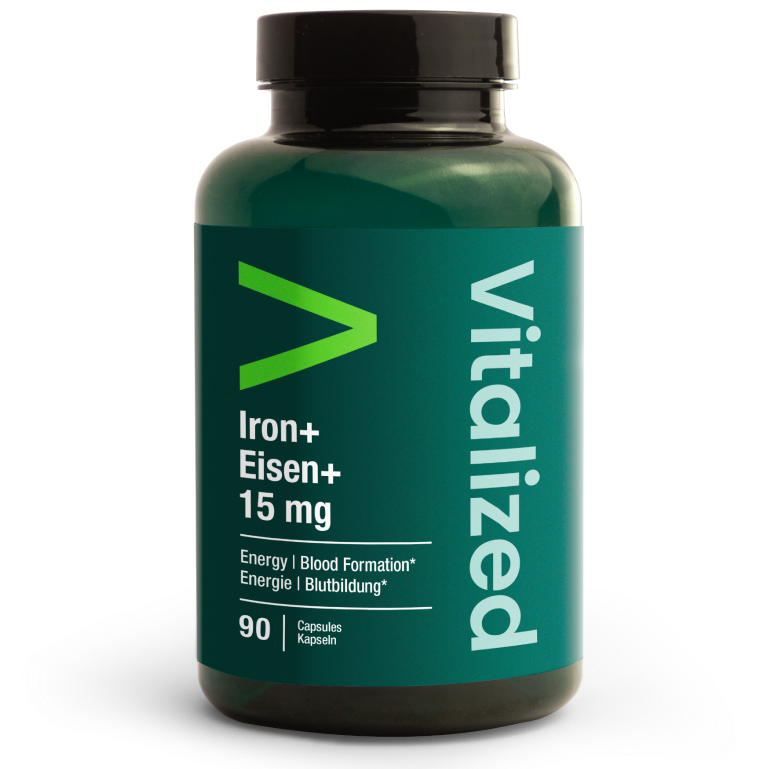 Vitalized Iron+ / Eisen+ 15 mg; tummanvihreä lieriömäinen muovipullo mattapinnalla, tekstillä Vitalized, sisältää 90 kapselia Iron+ Eisen+ 15 mg -ravintolisää; etiketissä englannin- ja saksankielinen teksti modernilla groteskifontilla; neutraali ja tasaisesti valaistu tausta, tuote keskitettynä kuvaan; ei ihmisiä tai käsiä.