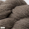 Close-up of three skeins of brownish-gray alpaca yarn with a matte, soft texture. Each skein is loosely wound and cylindrical. A small label in the lower left corner says hiekka in simple, sans-serif font. The background is plain and neutral. No packaging visible other than the label. No people or hands shown.