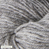 Close-up of gray yarn with a soft texture, showing its twisted fibers. The yarn is matte, loosely wound, and fills most of the frame. A small white label in the bottom left corner displays the word “keskiharmaa” in simple, black sans-serif text. There is no packaging visible. The background appears neutral and uncluttered.