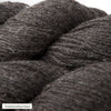 Close-up of dark gray wool yarn with a slightly coarse texture. The material is matte with visible fibers and a round, bundled form. A small white label in the corner shows plain, sans-serif text: tummanharmaa. Background is neutral and uncluttered. No hands or people visible in the image.