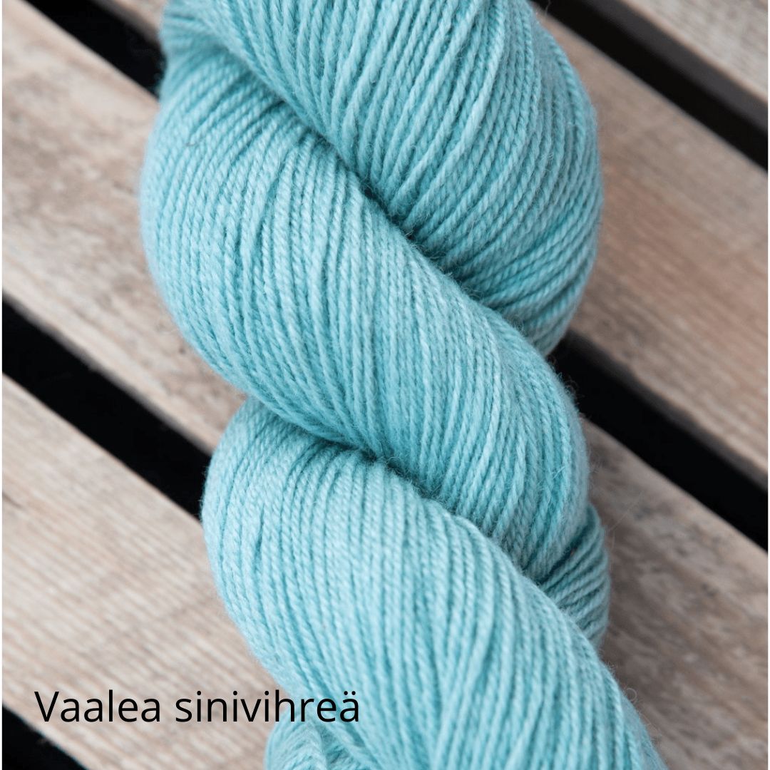 A skein of light blue-green yarn rests on wooden slats. The yarn is wound in a classic hank shape, with a matte finish and no visible packaging. The text “Vaalea sinivihreä” appears in the bottom left corner in clear, white sans-serif font. No people, hands, or actions are visible. Shot is taken from above against a wooden background.