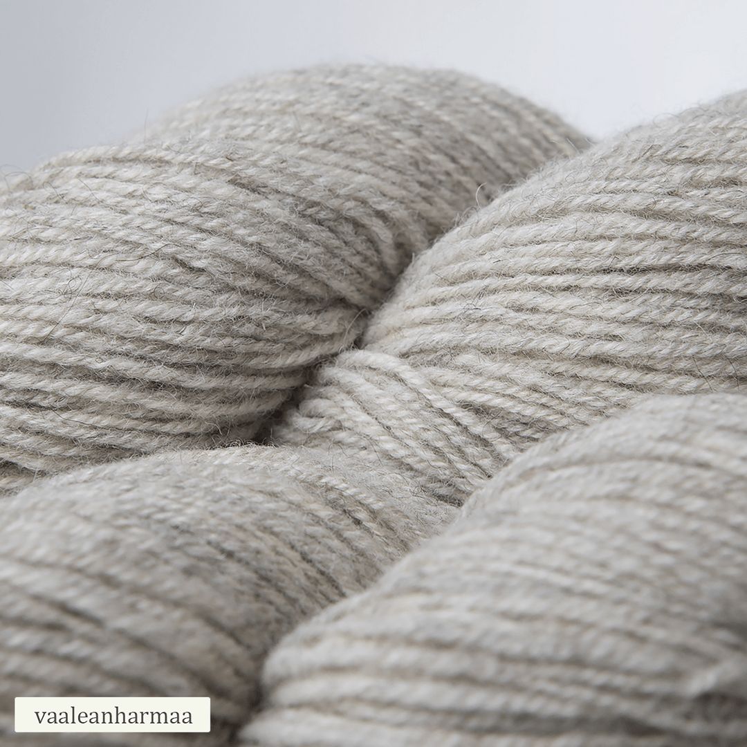 Close-up of light gray yarn skeins with a soft texture. The yarn is wound into oval skeins without additional packaging or bands. The surface appears matte and the fiber strands are visibly soft. The background is plain white. There is a small rectangular label in one corner with the word “vaaleanharmaa” printed in simple, sans-serif font.