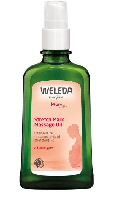 A green glass bottle of Weleda Stretch Mark Massage Oil with a white plastic pump dispenser; the bottle has a rectangular shape and glossy finish. The label is pink with white text, shows the silhouette of a pregnant woman, and reads “for all skin types.” The photo is taken against a plain white background. No people or hands present. A green bottle of Weleda Stretch Mark Massage Oil with a white pump, labeled for all skin types, features a pinkish label and the silhouette of a pregnant woman. Ideal as a