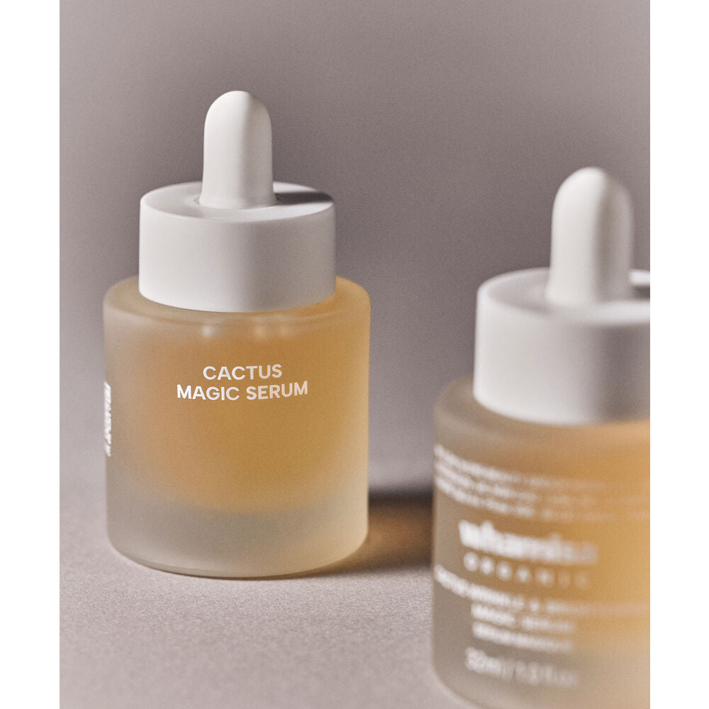 Whamisa Cactus Wrinkle & Brightening Magic Serum; kaksi huurrelasista tippapulloa kellertävää nestettä sisältäen, esillä pehmeällä neutraalilla taustalla; lieriömäiset pullot mattapintaisia, kirkkaat tipoittimet valkoisin korkein; etumaisessa pullossa luettava teksti ”CACTUS MAGIC SERUM” yksinkertaisella groteskifontilla; ei ihmisiä tai muita esineitä näkyvissä.