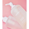 Whamisa Organic Flowers Cleansing Oil; kaksi Whamisa Organic Flower Cleansing Oil -pulloa valkoisin pumpuin vaaleanpunaisella taustalla, toinen pystyssä ja toinen kyljellään; pullot läpikuultavia huurretuin, mattapintaisin lieriömäisin muodoin; pakkauksessa valkoista kukka-aiheista tekstiä sekä englanniksi että korealaisin kirjaimin; ei ihmisiä tai käsiä kuvassa.