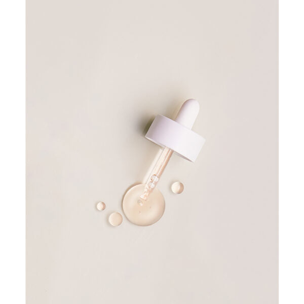 Whamisa Organic Flowers Facial Oil Deep Rich; valkokorkkinen tippapipetti lepää vaalealla pinnalla, ympärillä kirkkaita seerumipisaroita; pipetin putki läpinäkyvä ja lieriömäinen, ei näkyvää brändäystä tai tekstiä; korkki sileä ja läpikuultamaton muovia; tausta yksivärinen ja tasainen ilman kuvioita tai esineitä; ei ihmisiä tai käsiä kuvassa; kuva otettu ylhäältä.