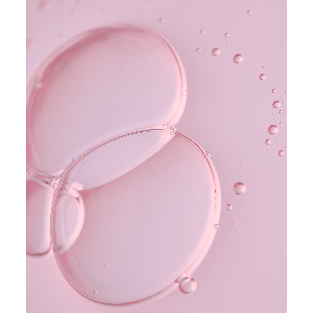 Whamisa Organic Flowers Toner Deep Rich; lähikuva läpikuultavista vaaleanpunaisista kuplista, jotka limittyvät vaaleanpunaisella pinnalla, ympärillä pienempiä helmiäishohtoisia kuplia; kuplat pyöreitä ja vaihtelevan kokoisia; tausta sileä ja yksivärinen; ei näkyvää pakkausta, tekstiä tai etikettejä, ei ihmisiä tai käsiä; kokonaisvaikutelma pehmeä ja abstrakti.