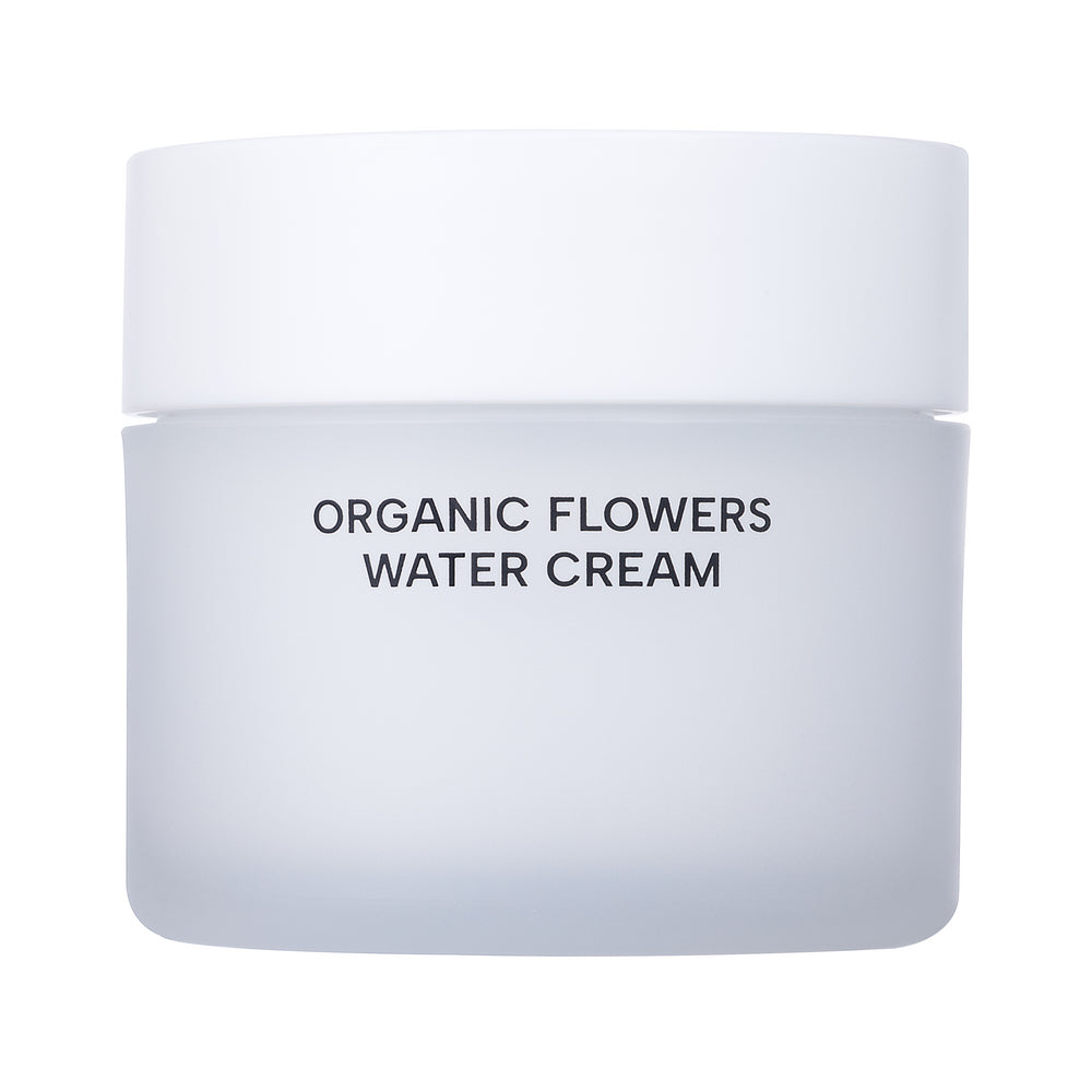 Whamisa Organic Flowers Water Cream; huurrevalkoinen purkki valkoisella kannella tekstillä ”ORGANIC FLOWERS WATER CREAM” etusivulla, mainita luonnonmukaisista ainesosista, aseteltuna tasaiselle valkoiselle taustalle; purkki pyöreä ja läpikuultamaton mattapinnalla; etikettiteksti yksinkertaisin groteskiversaalein; ei ihmisiä, käsiä tai toimintaa kuvassa; suoraan edestä otettu tuotekuva.