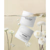 Whamisa Organic Flowers Water Cream; kaksi valkoista, pyöreää purkkia mattapinnalla ja kierrekannella tekstillä ”Whamisa Organic Flowers Water Cream”, osittain upotettuna kirkkaaseen veteen; purkkien ympärillä keltaisia ja valkoisia krysanteemikukkia; kaikki elementit pehmeällä beigellä saumattomalla taustalla tai sen heijastuksena; ei ihmisiä tai käsiä kuvassa.