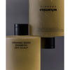 Whamisa Organic Seeds Shampoo Dry Scalp; kaksi beigeä Whamisa Organic Seeds Shampoo -pulloa kuivalle päänahalle, rikastettu luonnonaineksin, esillä lähikuvassa; pullot mattamuovia mustin läppäkorkein; kummassakin niukkaa etusivun tekstiä yksinkertaisella groteskityylillä; toinen pullo pystyssä, toinen ylösalaisin tasaisella taustalla.