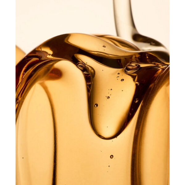Whamisa Organic Seeds Shampoo Dry Scalp; kultaista hunajaa valuu paksuina, kiiltävinä virtoina, joissa näkyvissä ilmakuplia; ei pakkausta tai etikettejä näkyvissä; tausta neutraali ja siisti; tuotteen pinta sileä ja kiiltävä, väriltään kultainen; ei ihmisiä, käsiä tai toimintaa kuvassa; lähikuva keskittyy nesteen tekstuuriin.