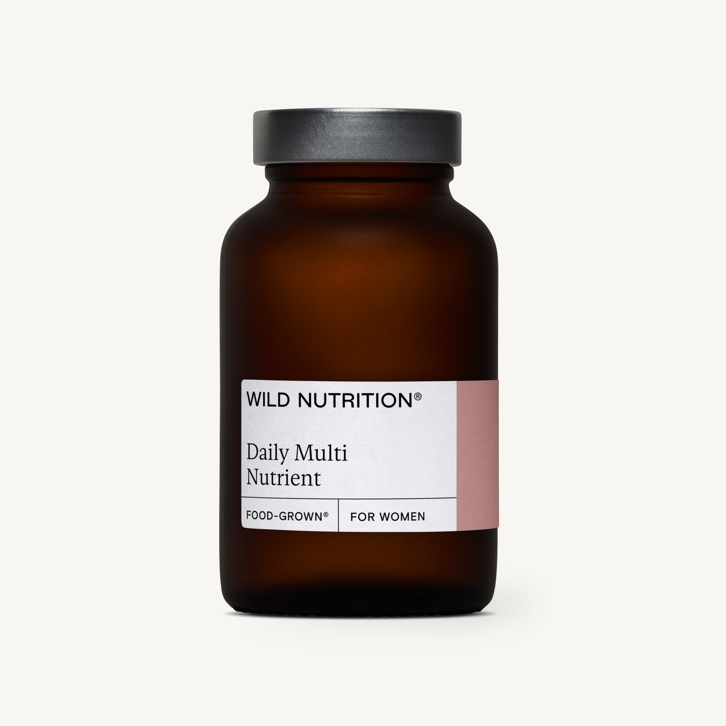 Wild Nutrition Daily Multi Nutrient, Food-Grown for Women -pullo, ruskea lasipullo mustalla korkilla valkoista taustaa vasten; pullo sylinterimäinen mustalla mattapintaisella kierrekorkilla; etiketti valkoinen lihavoidulla mustalla tekstausvapaalla tekstillä ja pienemmällä harmaalla alatekstillä; ei ihmisiä tai rekvisiittaa näkyvissä; kuva suoraan edestä valaistu.