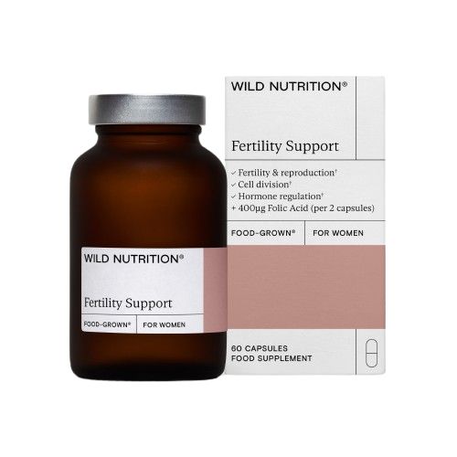 Fertility Support -pullo Wild Nutritionilta valkoisen ja vaaleanpunaisen pakkauksen vieressä, joka korostaa hyötyjä kuten hormonitasapainoa ja 400 µg foolihappoa; sekä pullo että pakkaus siistiä tekstausvapaata typografiaa; pakkaus mattapinnalla, osassa lihavoitua tekstiä; ei ihmisiä tai käsiä näkyvissä kuvassa; tausta yksinkertainen.