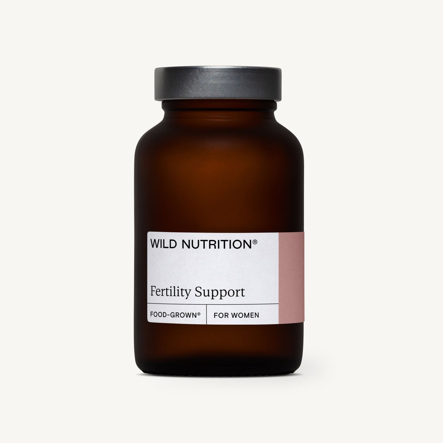 Wild Nutrition Fertility Support -pullo, ruskea lasipullo mattametallisella kannella, sylinterimäinen muoto ja valkoinen suorakulmainen etiketti, keskitettynä sileälle vaalealle taustalle; etiketissä lukee "Wild Nutrition Fertility Support, Food-Grown" ja "For Women" tekstausvapaalla fontilla; ei ihmisiä tai käsiä näkyvissä; suora edestäpäin otettu tuotekuva.
