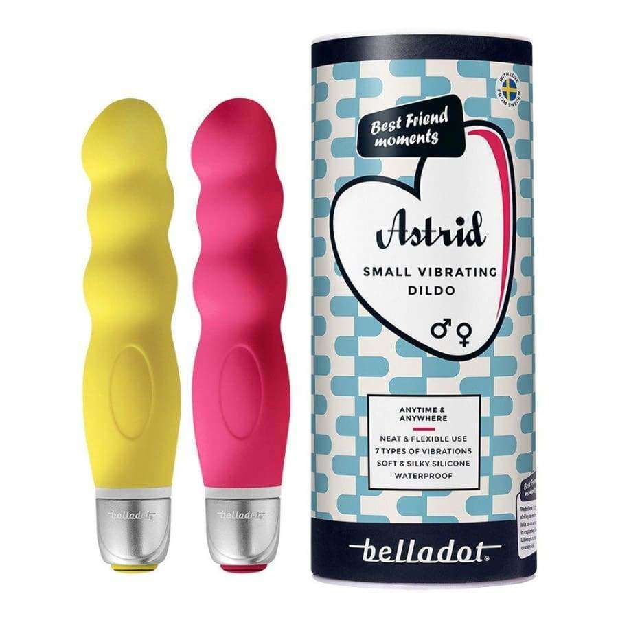 Belladot Astrid Small Vibrating Dildo: kaksi aaltomaista silikonivibraattoria keltaisena ja vaaleanpunaisena mattapinnalla seisoo pystyssä sylinterimäisen pahvipakkauksen vieressä; pakkauksessa teksti "Astrid Small Vibrating Dildo by belladot" selkeällä groteskikirjasimella; pakkauksessa myös sydämenmuotoinen kuvitus; ei ihmisiä tai käsiä näkyvissä, tausta on neutraali.