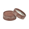 A round, brown box with a decorative white pattern and a partially open lid reveals a soft interior adorned with an intricate butterfly design. The box is matte and constructed from cardboard or similar material. No visible typography or legible text. It sits against a plain, neutral background in a close-up product shot. No people or hands are present.