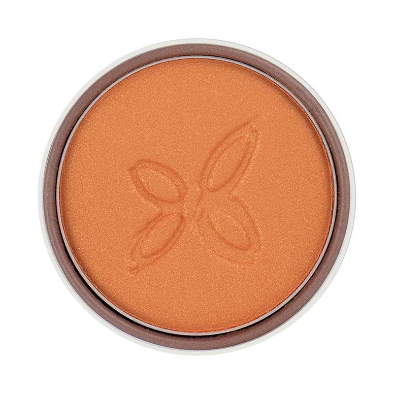 A round compact of shimmery orange powder makeup featuring a subtle embossed butterfly design in the center. The powder surface is smooth with a metallic sheen. Packaging is circular and plastic, color not specified. No visible typography or label text on product or packaging. Product placed against a plain, neutral background; no people or hands present in the image. Studio shot, close-up view.