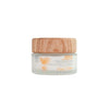 A small glass jar of Feel Free Vitamin C Hydrating Age Vitamin Booster Cream with a wooden lid and a minimalist leaf design on the label provides hydrating benefits with vitamin C. The jar is clear with a cylindrical shape, matte wooden screw-top lid, and white label featuring simple sans-serif text and green graphics. The background is plain white. No people or hands visible; frontal product shot.