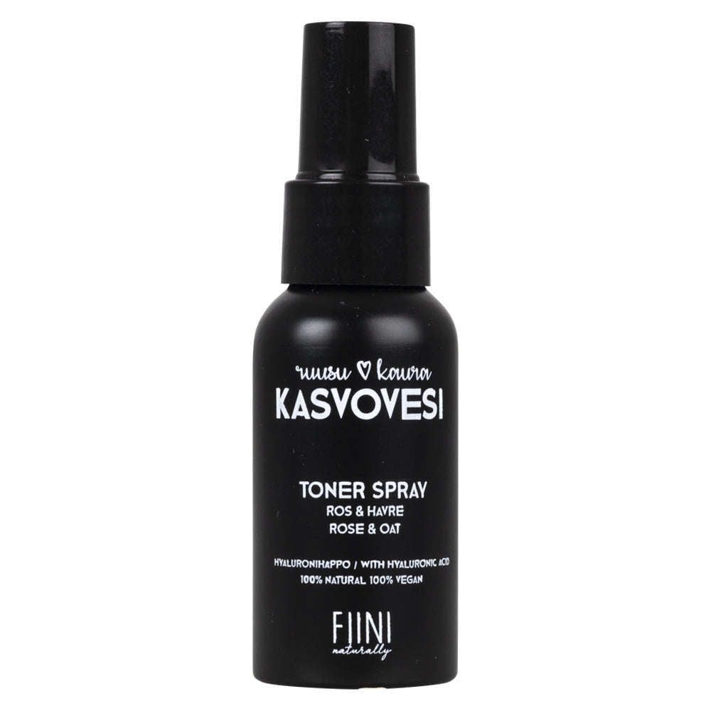 Fiini Naturally Ruusu-Kaura Kasvovesi; musta muovinen suihkupullo mattapintaisena, musta suutin ja kirkas korkki; etuetiketissä yksinkertainen valkoinen ja beige groteskikirjasin, teksti "KASVOVESI Toner Spray Rose & Oat by Fini Naturally"; mainitsee hyaluronihapon, 100-prosenttisen luonnollisuuden, vegaanisuuden ja kauran rauhoittavat hyödyt; vaalea tausta, keskitetty studiokuva ilman ihmisiä tai käsiä.