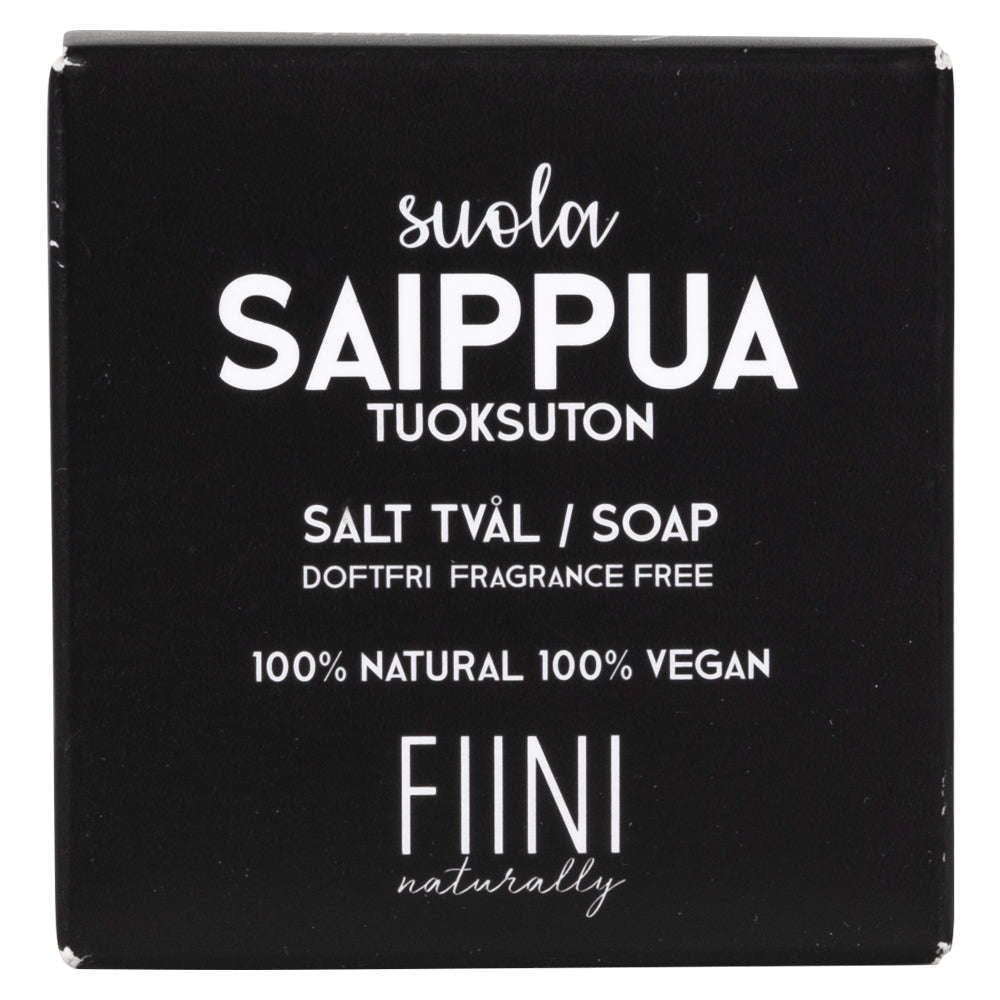 Fiini Naturally Suolasaippua Tuoksuton; musta suorakulmainen mattapintainen pakkaus vaalealla taustalla; etiketissä yksinkertainen valkoinen groteskiteksti, joka kertoo tuotteen olevan tuoksuton, 100-prosenttisesti luonnollinen ja vegaaninen, tekstit suomeksi, ruotsiksi ja englanniksi; ei ihmisiä tai muita esineitä kuvassa.