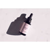 FLOW Cosmetics Arctic Beauty Oil -tiputinpullo tummaa lasia, lepää vaalealla pinnalla pehmeän varjon kanssa; lieriömäinen, musta kierrekorkki ja kiinteä tiputin; etiketissä vähän, selkeää tekstiä; tausta tekstuuriton valkoinen; kuvassa vain tuote, ei rekvisiittaa tai ihmisiä.