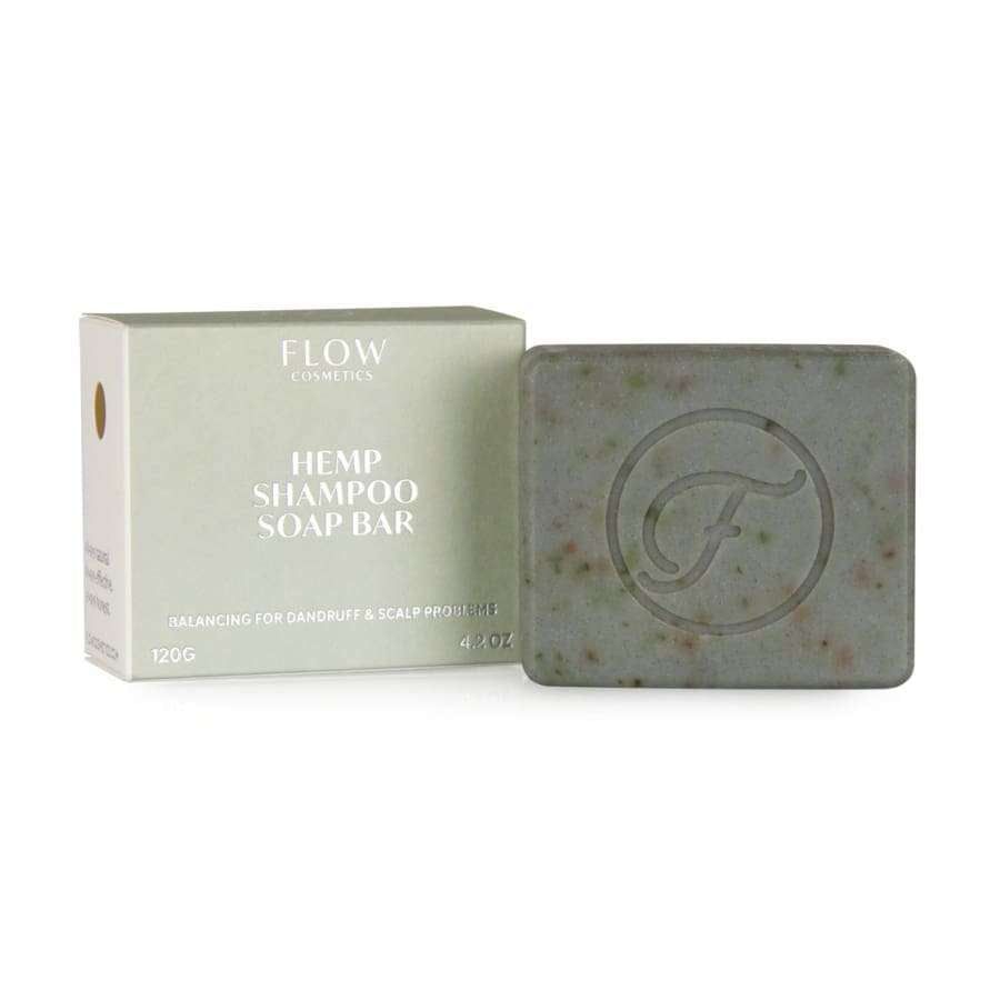 Flow Cosmetics Hemp Shampoo Soap Bar, 120 g; vihertävä, neliömäinen saippuapala, jossa kohokuvioitu "F"-kirjain, pakkauksen vierellä beige, suorakulmainen rasia tekstillä "Flow Cosmetics"; rasiassa kerrotaan hilseen ja hiuspohjan ongelmien luonnollisesta hoidosta; saippuapala mattapintainen ja kiinteä; ei käsiä tai ihmisiä, vaalea tausta.