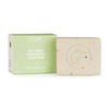 Flow Cosmetics Tea Tree Shampoo Soap Bar; vaaleanvihreä rasia beigen saippuapalan vieressä, jossa kohokuvioitu pyöreä "F"-logo; pakkaus korostaa teepuuöljyn virkistäviä ominaisuuksia; rasiassa yksinkertaista mustaa groteskitekstiä kahdella painolla; molemmat mattapintaisia ja suorakulmaisia siistein reunoin; ei ihmisiä tai käsiä; tausta kauttaaltaan vaalea, ei lisärekvisiittaa.