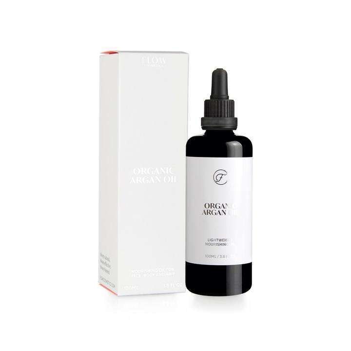 Luomu-argan-öljy tiputinkorkilla, pullo pakkauksensa vieressä; lasinen, lieriömäinen pullo, mattamusta tiputin; sekä pullossa että rasiassa minimalistinen mustavalkoinen etiketti groteskifontilla, kertoo sisällön ja tuotetyypin; vaalea, kirkas tausta; ei ihmisiä tai käsiä.