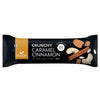 A Foodin protein bar labeled Crunchy Caramel Cinnamon, featuring images of cinnamon sticks, caramel pieces, and cashews on a sleek black wrapper. Wrapper color is black with photo-realistic graphics. Label includes 13g plant-based protein and 50g weight. Packaging has a rectangular shape with sealed ends. No people or background objects are visible in the image.