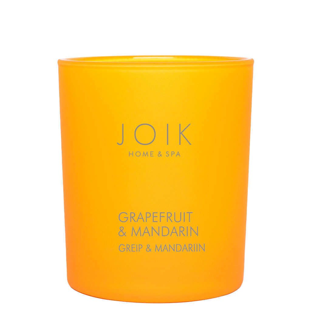 A bright orange candle in a clear glass cylindrical jar with a glossy finish, labeled JOIK HOME & SPA in black sans-serif font. The label is rectangular and placed on the front of the jar. The background is plain white, and no people or hands are present. The shot is a product-focused, straight-on view.