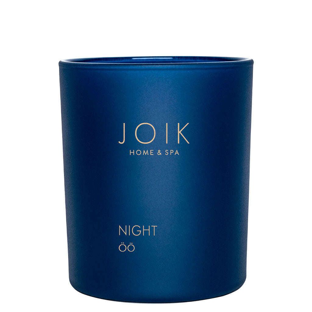 A dark blue soy candle jar labeled JOIK HOME & SPA with NIGHT and öö written below in gold text. Jar is round with straight sides and a matte finish, no visible lid or outer packaging. Label uses uppercase sans-serif font for main text, smaller type for subtext. The setting is a plain white background. No people or hands are present in the image.