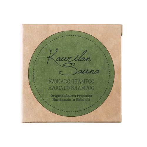 Kaurilan Sauna Palashampoo Avokado; ruskea pakkaus suurella pyöreällä vihreällä etiketillä tekstillä "Kaurilan Sauna Avokado Shampoo, alkuperäiset saunatuotteet, käsintehty Helsingissä", korostaen avokadon ravitsevia hyötyjä; pakkaus suorakulmainen mattapintaisena, teksti valkoisella groteski- ja kaunokirjoituskirjasimella; vaalea tausta, ei ihmisiä tai käsiä kuvassa.