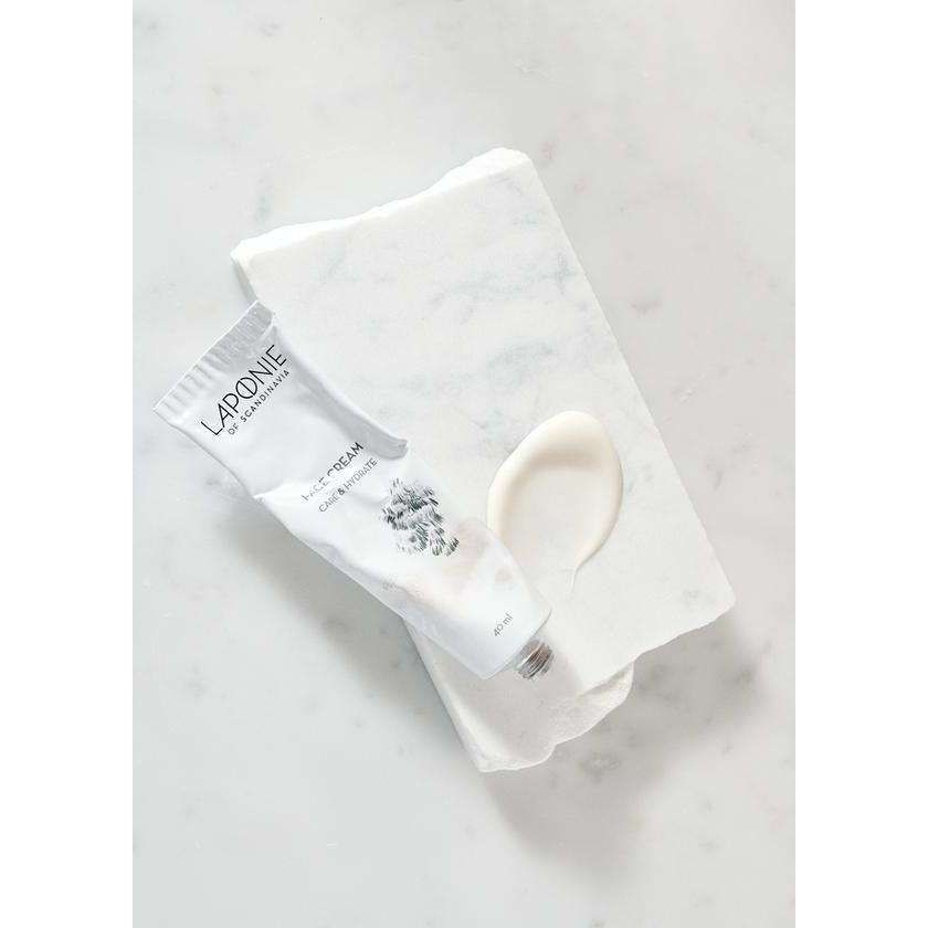 Laponie of Scandinavia Kasvovoide; valkoinen tuubi tekstillä "La Pruné vegan skincare cream" suorakulmaisella marmorialustalla; tuubi sileää mattapintaista muovia mustalla groteskitekstillä; vieressä pieni nokare valkoista voidetta marmorilla; tausta ja alusta kiillotettua valkoista marmoria; ylhäältä kuvattu tasaisesti valaistu tuotekuva, ei ihmisiä tai käsiä.