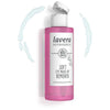 Lavera Soft Eye Silmämeikinpoistoaine; vaaleanpunainen ja valkoinen muovipullo Lavera Soft Eye Make-Up Remover -tuotetta valkoisella läppäkorkilla; pullo sylinterinmuotoinen sileän mattapintaisena; sinistä nestettä pirskeinä ympäröi tuotetta pelkistetyllä taustalla; etiketissä selkeä groteskikirjasin ja maininta luomualoe verasta sekä hellävaraisesta puhdistuksesta; ei ihmisiä tai käsiä kuvassa.