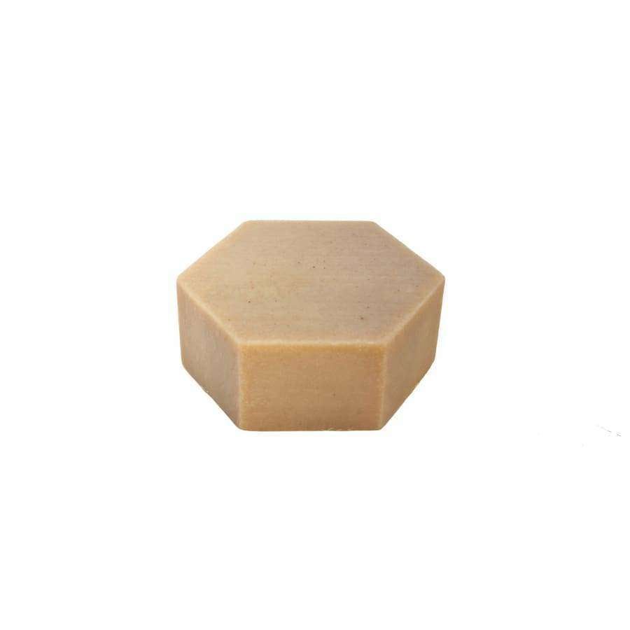 Kuusikulmainen beige käsintehdyn saippuan palikka seisoo pystyssä valkoisella taustalla; mattapintainen ilman näkyvää pakkausta tai etikettiä; ei näkyvää typografiaa; studiokuva suoraan edestä otettuna; ei ihmisiä tai käsiä kuvassa.
