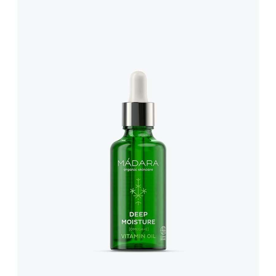 Madara Deep Moisture Vitamiiniöljy; vihreä lasinen tiputinpullo tekstillä "MÁDARA organic skincare Deep Moisture Vitamin Oil" pystyssä; pullo lieriömäinen kiiltäväpinnalla, päällä valkoinen tiputinkorkki; typografia valkoista ja groteskia, selkeästi painettu etuosaan; tausta vaalea ja tekstuuriton; ei ihmisiä tai käsiä kuvassa.