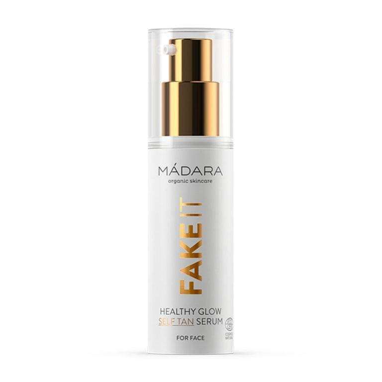 MÁDARA Organic Skincare FAKE IT Healthy Glow Self Tan Serum -itseruskettava kasvoseerumi; valkoinen muovipullo pystyssä, kultainen pumppu ja läpinäkyvä korkki; pullon pinta mattainen; etiketti groteskifontilla suuraakkosin mustana; vaalea, esineetön tausta; ei ihmisiä tai muita objekteja; ravitseva koostumus antaa iholle säteilevän, auringonpolttaman näköisen sävyn.