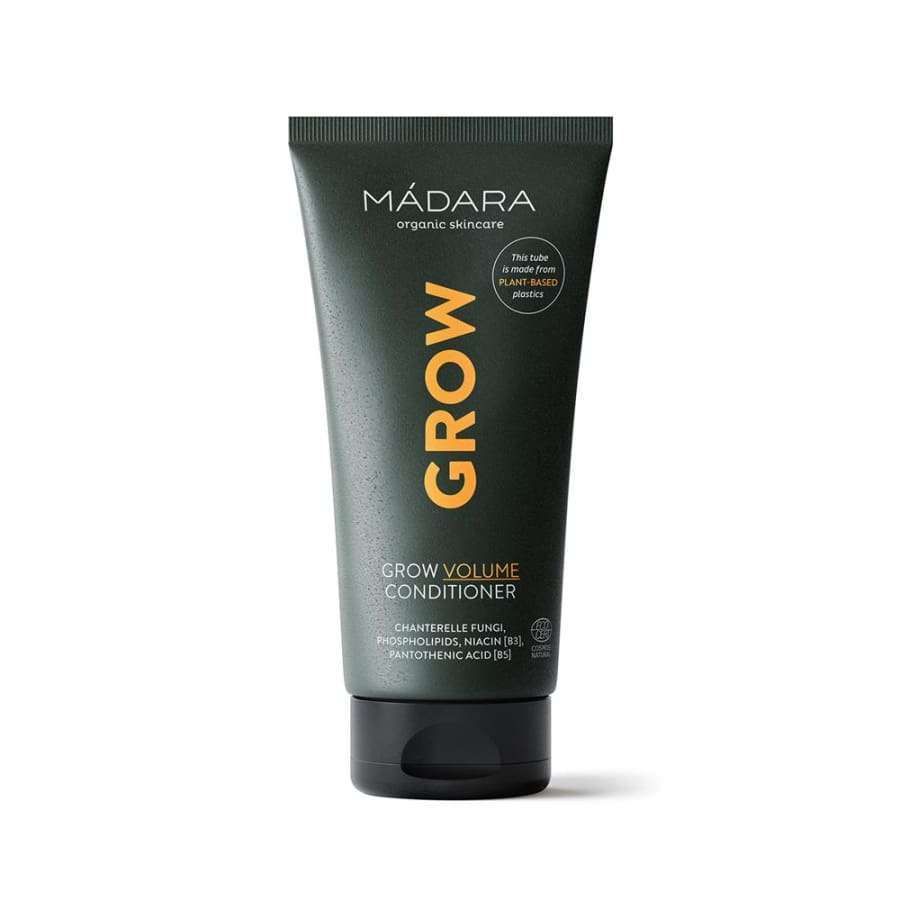 MÁDARA Grow Volume Conditioner -tuubi, tummanvihreä, oranssia ja valkoista kasviaiheista tekstiä, pystyssä valkoista taustaa vasten; tuubi sylinterimäinen muovia mattaviimeistelyllä, lihavoitua tekstausvapaata typografiaa oranssilla ja valkoisella; luettavassa etiketissä teksti "MÁDARA Grow Volume Conditioner" sekä kasviaiheisia graafisia elementtejä; ei ihmisiä tai käsiä näkyvissä.