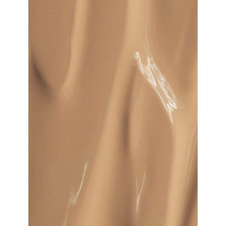 MÁDARA Skin Equal Meikkivoide, sävy Golden Sand; sileä, beige nestemäinen meikkivoide pehmein virtaavin juovin ja hienoisin kiiltokohdin, muistuttaen kermaista, säteilevää koostumusta; ei näkyvää pakkausta tai säiliötä; lähikuva neutraalilla taustalla; ei tekstiä, ihmisiä tai käsiä.
