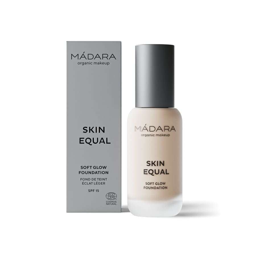 MÁDARA Skin Equal Soft Glow Foundation SPF 15, sävy Porcelain; pullo pystyssä harmaan suorakulmaisen rasian vieressä; pullo lieriömäinen, huurrettua lasia mattaefektillä, musta korkki; molemmissa mustaa ja valkoista groteskitekstiä tuotenimestä, brändistä ja SPF-luvusta; vaalea tausta, tasainen studiovalaistus.