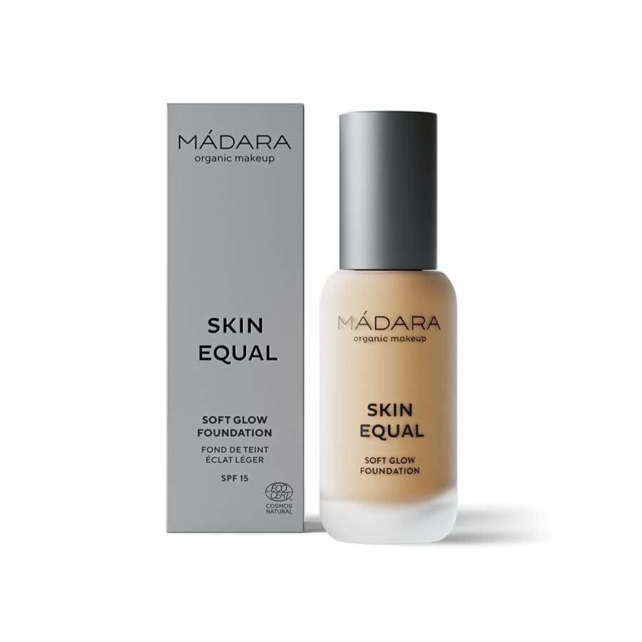 MÁDARA Skin Equal Soft Glow Foundation SPF 15, sävy Sand; lieriömäinen pullo mattabeigellä pinnalla, pystyssä harmaan rasian vieressä; molemmissa mustaa groteskitekstiä tuotenimestä, SPF-luvusta ja luomumeikistä; vaalea tausta, ei ihmisiä; lähikuva tuotteesta.